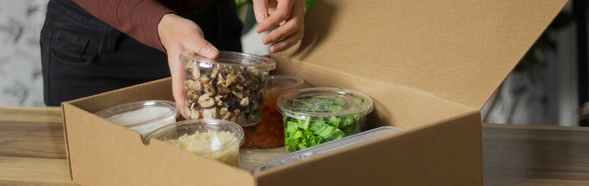 Des mains retirent des plats d'ingrédients d'une boite de carton